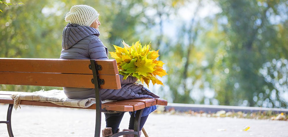 Senior woman sitting on a bench in the fall